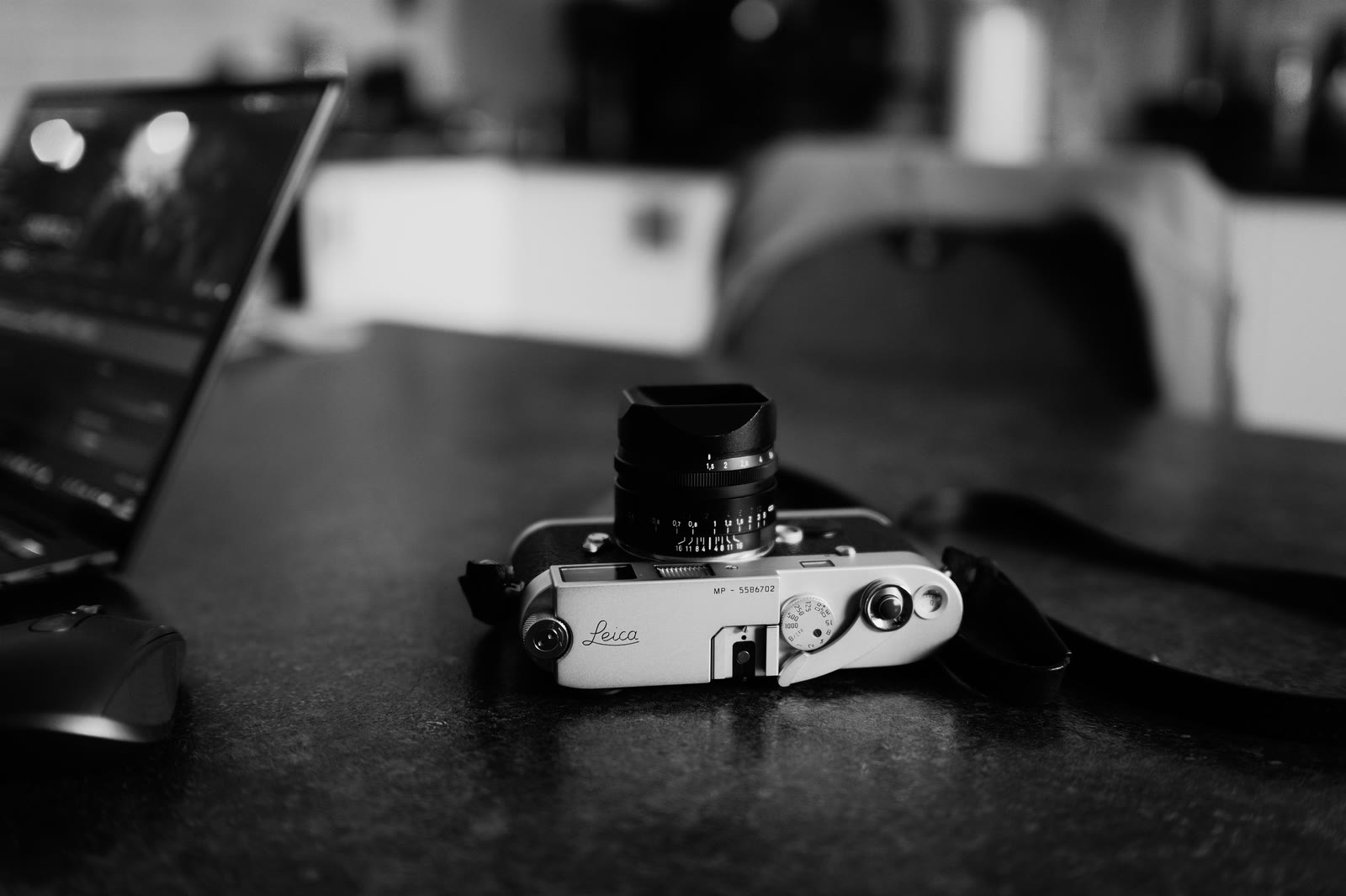 Câmera Leica sobre uma mesa de trabalho, ao lado de um notebook.