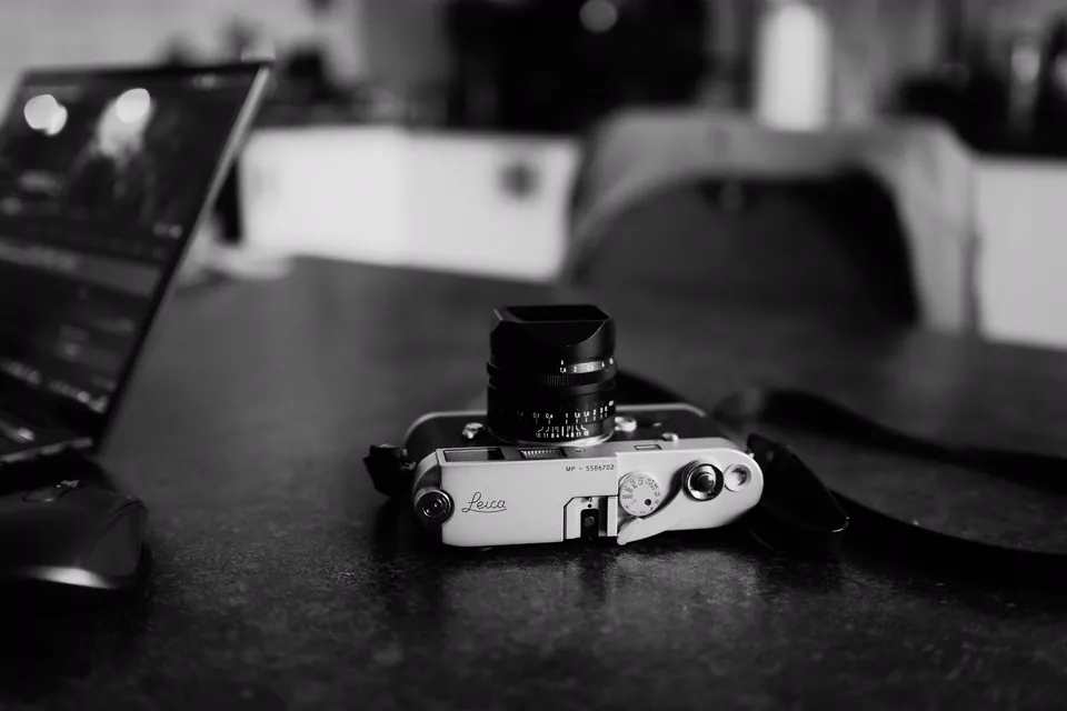 Câmera Leica sobre uma mesa de trabalho, ao lado de um notebook.